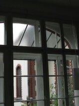 Fenster mit Blick auf einen Garten Ein Zimmer mit maßgefertigten Fenstern, durch die man auf einen grünen Garten und eine Ziegelstruktur im Hintergrund blickt.