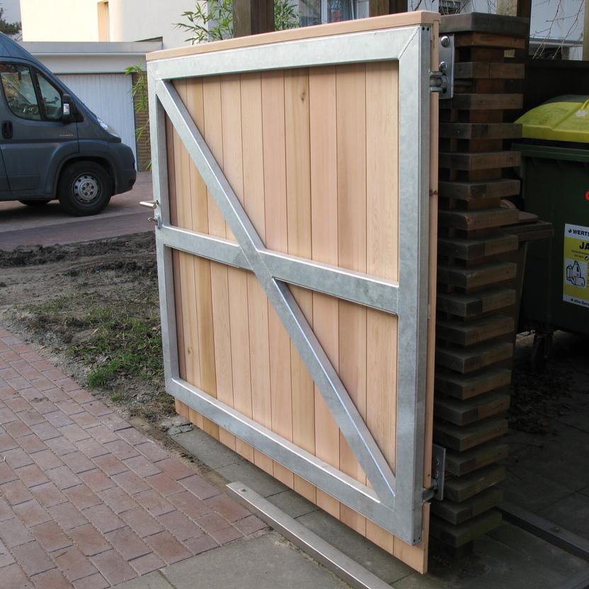 Robustes Holztor mit auff&auml;lligen Metallstreben in X-Form, auf einem gepflasterten Untergrund montiert.