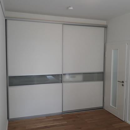 Moderner Schrank nach Maß in einem hellen Raum Großer, weißer Schiebetürenschrank nach Maß, der sich perfekt in den Raum einfügt. Ein Streifen aus satiniertem Glas setzt einen eleganten Akzent.