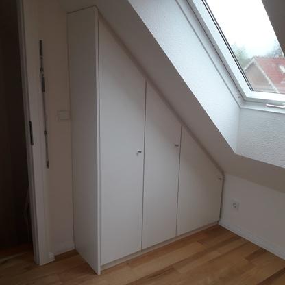 Maßgefertigter Wandschrank unter einer Dachschräge Weißer Wandschrank nach Maß, eingepasst unter eine Dachschräge mit Dachfenster, sorgt für effiziente Raumnutzung und helle Atmosphäre.