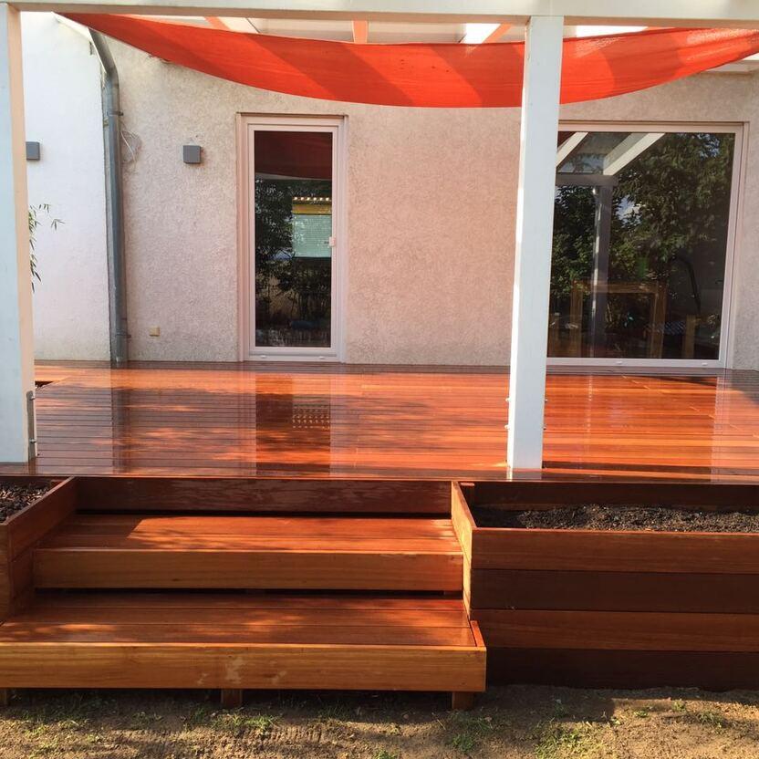 Maßgeschneiderte Terrasse mit Stufen und Sonnenschutz Glänzende Holzterrasse nach Maß mit mehrstufigem Zugang, weißer Überdachung und orangefarbenem Sonnensegel, ideal für entspannte Sommertage.