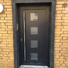 Moderne Tür nach Maß in einem Ziegelbau Elegante schwarze Tür nach Maß mit horizontalen Glaseinsätzen, eingefasst in einen gelben Ziegelrahmen, bietet einen modernen Eingangsbereich.