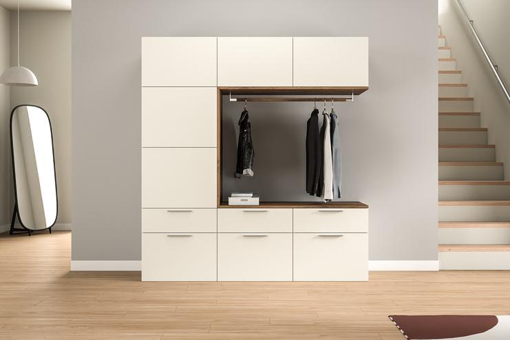 Moderner, maßangefertigter Garderobenschrank im Eingangsbereich. Ein maßgefertigter Garderobenschrank in Cremeweiß mit Holzakzenten bietet eine elegante Aufbewahrungslösung im Eingangsbereich, inklusive einer Kleiderstange und Stauraum.