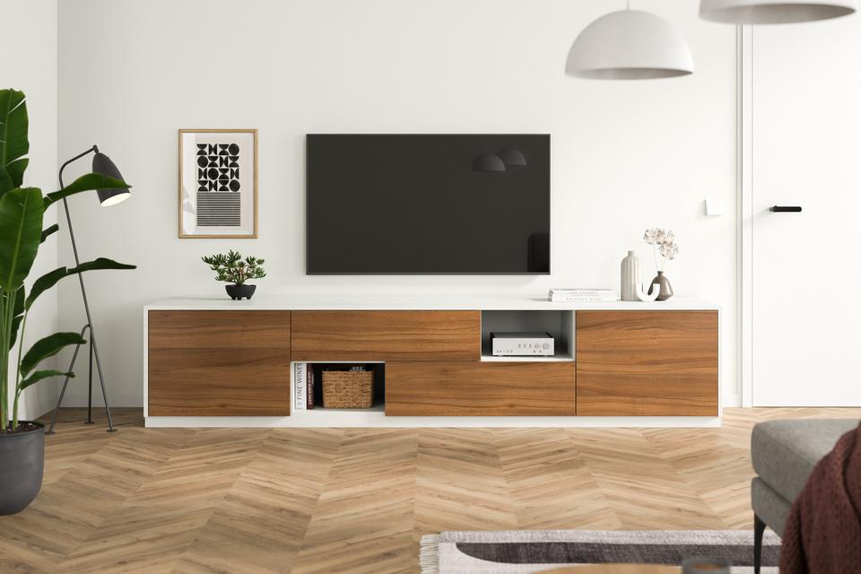 Eine minimalistische Kommode nach Maß, mit Holzelementen und weißen Fronten, steht unter einem Wand-TV, umgeben von stilvoller Dekoration.